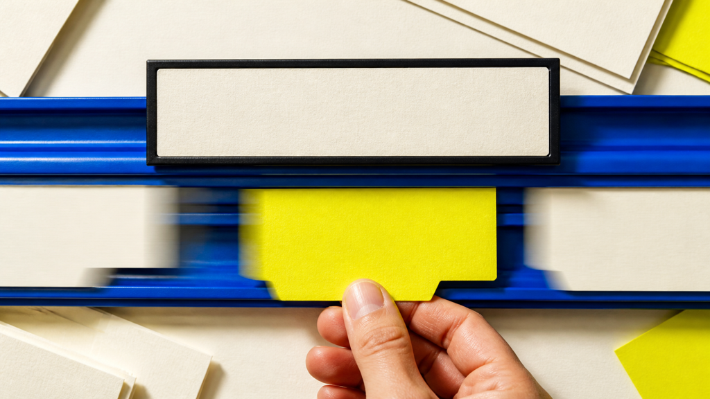 A fixed office nameplate sits above moving blue task cards while a hand holds one acid-yellow responsibility card.
